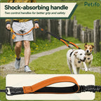 Owner walking two dogs on a trail using a durable orange dual-dog leash with a shock-absorbing handle.