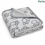 Angled view of a folded grey and white paw print pet blanket resting on a clean white surface.
