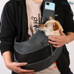Person carrying a small dog securely inside a grey mesh hands-free pet sling.