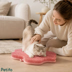 A woman gently petting a cat as it stretches out and rubs against a pink silicone self-grooming pad on the floor.