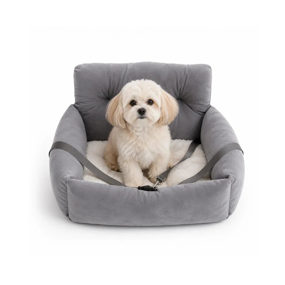Small white and brown puppy sitting inside a plush grey dog car seat with a secure black safety harness strap.
